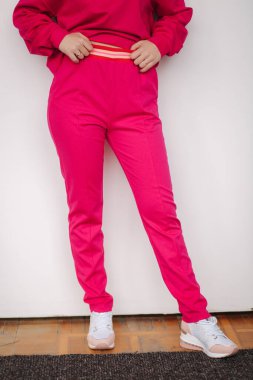 Pembe eşofmanlı çekici genç bir manken. Stüdyoda kıyafet sergileyen bir kadın. Beyaz arkaplan