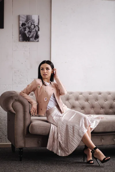 Vacker brunett kvinna visar vårkläder i studio. Modellen sitter på soffan. Vit bakgrund — Stockfoto