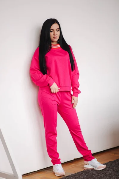 Attractive young model in pink tracksuit. Woman demonstrating clothes in studio. White background