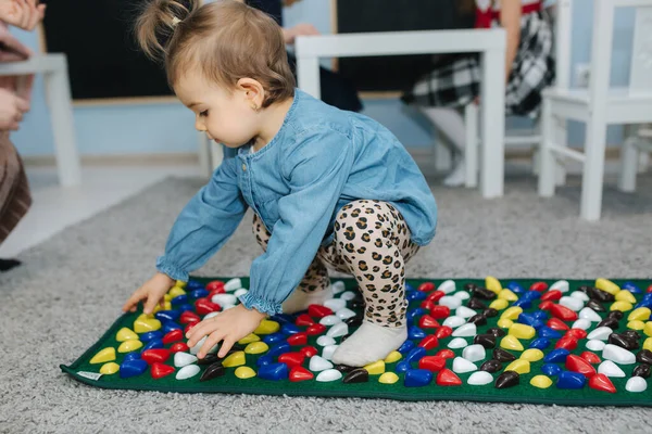 Niña jugar en la alfombra de juego con piedras. Alfombra para masaje de pies — Foto de Stock