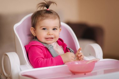 Küçük tatlı kız, gece sandalyesinde yemek yiyor. Evde gülümseyen küçük bir çocuğun portresi