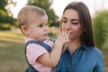 Dışarıda annesinin ellerinde şirin bir bebek var. Aile yazın parkta olur. Denim tarzı. Kotlu anne ve kızı.