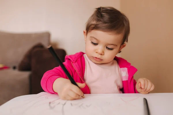 Menina feliz sentar-se à mesa e wthire algo. Menina usar lápis para desenhar em papel branco em casa — Fotografia de Stock