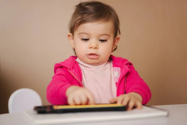 Щаслива дівчинка сидить за столом і щось шикарне. Маленька дівчинка використовує олівець для малювання на білому папері вдома — стокове фото