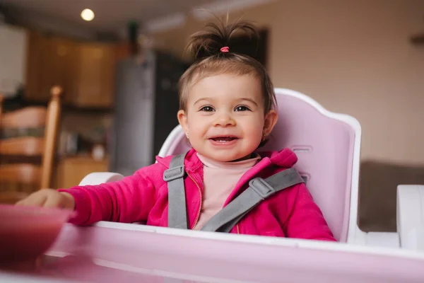 Pequeña niña linda están comiendo en silla alta. Retrato de un niño sonriente en casa — Foto de Stock