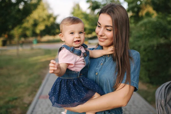 Bel bambino sulle mani delle mamme fuori. Famiglia nel parco in estate. Stile denim. Mamma e figlia in jeans — Foto Stock