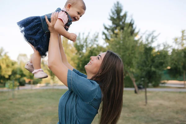 Słodkie dziecko na rękach mamy na zewnątrz. Rodzina w parku latem. W stylu dżinsów. Mama i córka w dżinsach — Zdjęcie stockowe