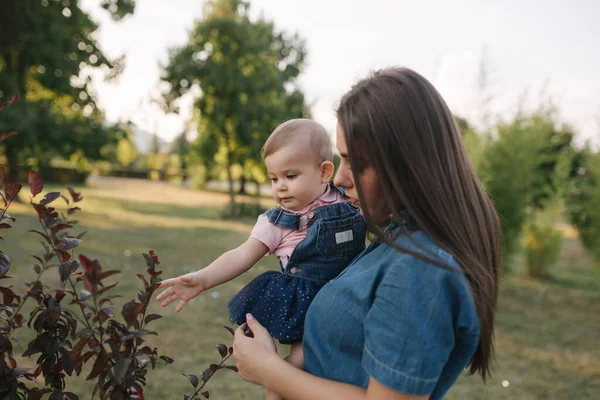 Милый ребенок на маминых руках снаружи. Семья в парке летом. Джинсовый стиль. Мама и дочь в джинсах — стоковое фото