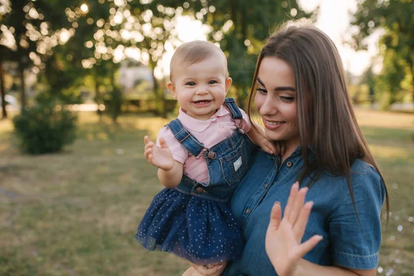 Aranyos baba az anyukák kezén odakint. Család a parkban nyáron. Farmerstílusban. Anya és lánya farmerben. — Stock Fotó