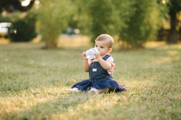 Bebé bebe agua del biberón afuera en el parque. Bebé gir sentarse en la hierba — Foto de Stock