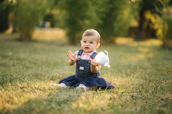 Bebé bebe agua del biberón afuera en el parque. Bebé gir sentarse en la hierba — Foto de Stock