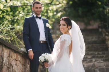 Güzel gelini ve yakışıklı damadı düğün gününde dışarıda yürüyor. Mutlu yeni evliler.