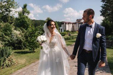 Güzel gelini ve yakışıklı damadı düğün gününde dışarıda yürüyor. Mutlu yeni evliler.
