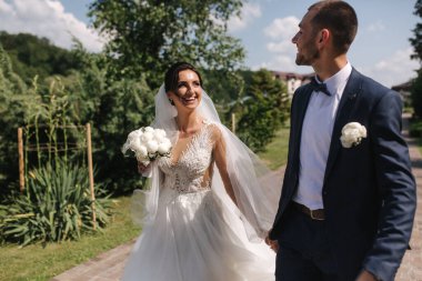 Güzel gelini ve yakışıklı damadı düğün gününde dışarıda yürüyor. Mutlu yeni evliler.