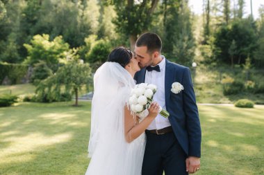 Güzel gelini ve yakışıklı damadı düğün gününde dışarıda yürüyor. Mutlu yeni evliler.