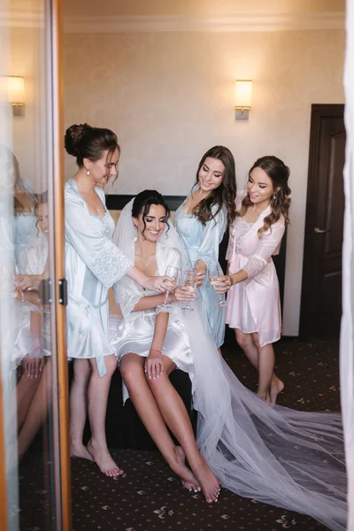 Hermosa novia con las mejores damas de honor bebiendo champán en el hotel. Mañana de novia. Sexy damas de honor en excitante negligee —  Fotos de Stock