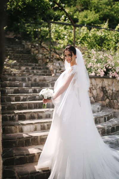 Vista posteriore della splendida sposa stare sulle scale in elegante abito da sposa con mazzo di fiori bianchi nel giorno del suo matrimonio — Foto Stock