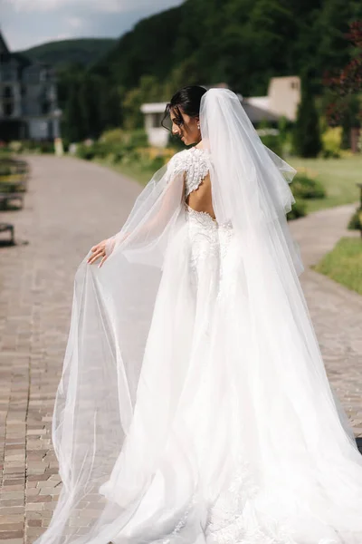 Vue arrière de magnifique mariée debout sur les escaliers dans une élégante robe de mariée avec bouquet de fleurs blanches dans son jour de mariage — Photo