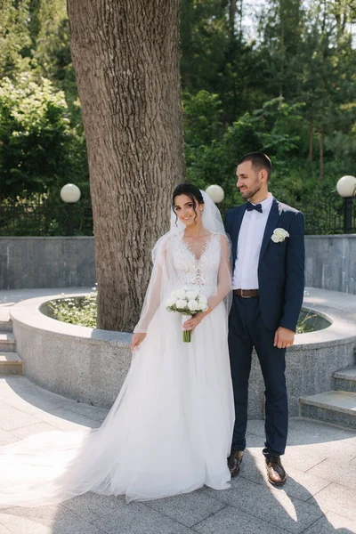 Krásná nevěsta se svým krásným ženichem kráčí venku v den svatby. Šťastní novomanželé — Stock fotografie