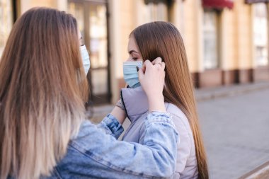 Maskeli kızlar. Coronavirus teması. Şehirdeki kadınlar karantina sırasında yürür. Maske takmaya yardım et