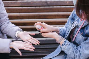 Koruyucu maskeli genç kadınlar el spreyi sıkarlar. Kadınlar dışarı.