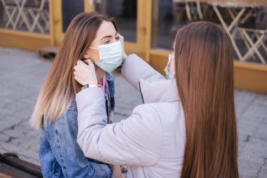 Maskeli kızlar. Coronavirus teması. Şehirdeki kadınlar karantina sırasında yürür. Maske takmaya yardım et