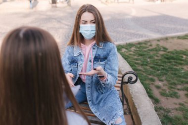 Maskeli kızlar. Coronavirus teması. Karantina sırasında şehir merkezindeki bankta oturan kadınlar