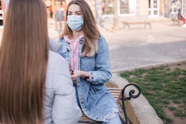 Maskeli kızlar. Coronavirus teması. Karantina sırasında şehir merkezindeki bankta oturan kadınlar