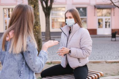 Maskeli kızlar. Coronavirus teması. Karantina sırasında şehir merkezindeki bankta oturan kadınlar