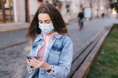 Maskeli kız. Coronavirus teması. Şehirdeki kadınlar, karantina sırasında. Şehirde tek başına. Kadın kullanıcı telefonu