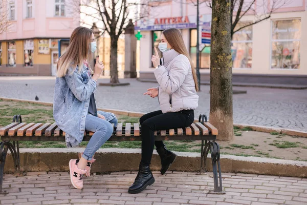 Mädchen in Masken. Coronavirus Thema. Frauen sitzen während der Quarantäne auf der Bank in der Innenstadt — Stockfoto