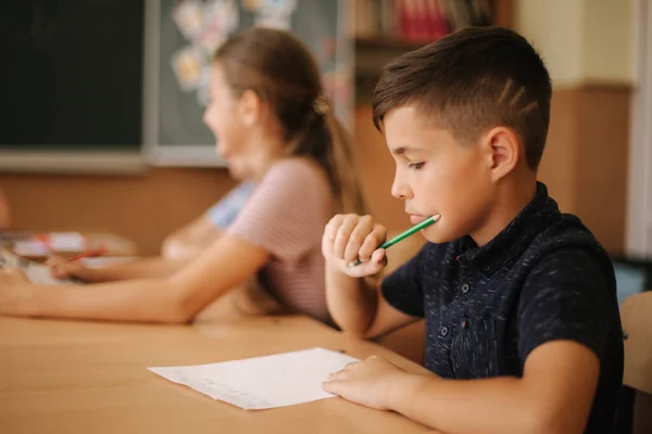 Oktatás, általános iskola. Tanulás és emberek koncepció - csoport az iskolás gyerekek tollak és notebook írás teszt az osztályteremben — Stock Fotó