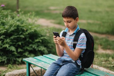 Genç bir çocuk karantina sırasında bankta oturup online oyunlar oynuyor.