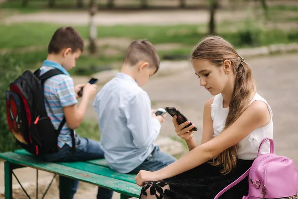 Двоє хлопчиків та дівчат користуються своїми телефонами під час шкільних канікул. Милі хлопчики сидять на лавці і грають в онлайн ігри — стокове фото