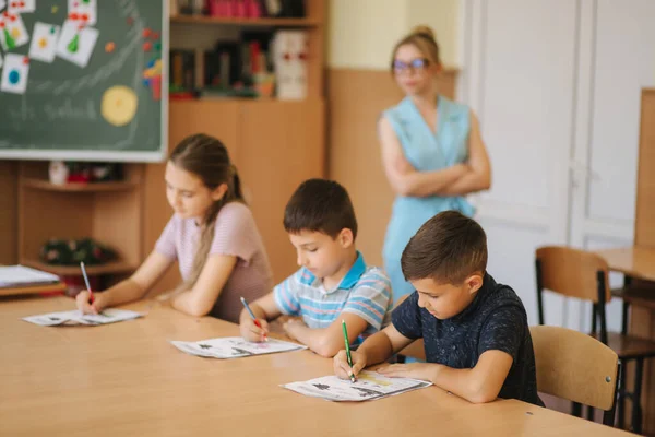 Professor ajudando crianças da escola a escrever teste em sala de aula. educação, escola primária, aprendizagem e conceito de pessoas — Fotografia de Stock