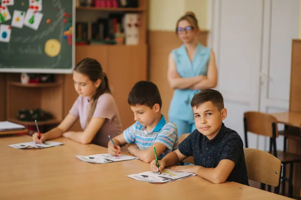 Учитель помогает школьникам писать тесты в классе. образование, школа, обучение и человеческая концепция — стоковое фото