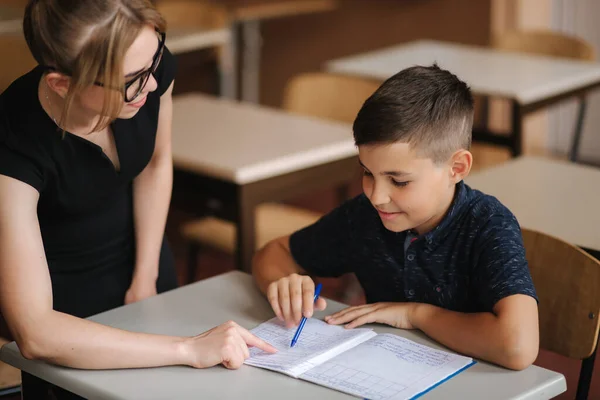 教師は学校の子供たちが教室でテストを書くのを助ける。教育や小学校学習や人々の概念は — ストック写真