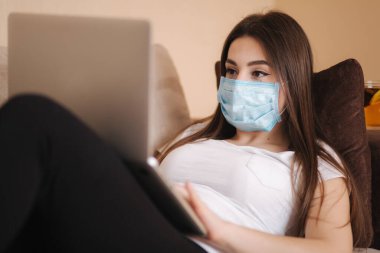 Coronavirus sırasında koruyucu maskeli bir kadın evden çalışıyor. Kadın kendini evde izole etmiş. Evde Kalın