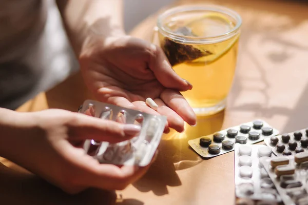 Primer plano de las manos de las mujeres toman pastillas. Mano con pastillas y té negro con limón. Inmunidad. Vitaminas — Foto de Stock