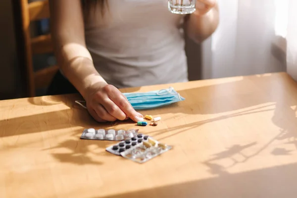 Una donna si toglie la maschera medica per prendere delle pillole. Femmina a casa in quarantena. Auto isolamento. Helthy donna prendere vitamine — Foto Stock