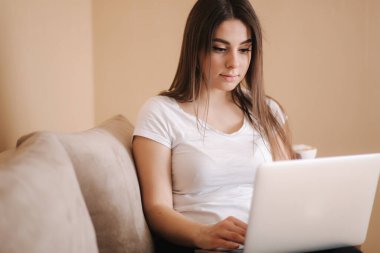 Genç bir kadın karantinada çalışıyor. Kadınlar kanepede dizüstü bilgisayar kullanır. Kadın uzaklık öğrenimi