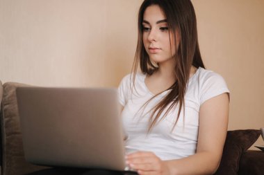 Genç bir kadın karantinada çalışıyor. Kadınlar kanepede dizüstü bilgisayar kullanır. Kadın uzaklık öğrenimi