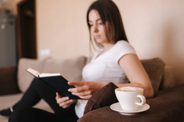 Young attractive woman read the book at home. Quarantine time. Woman drink cappuchino and fill the notebook