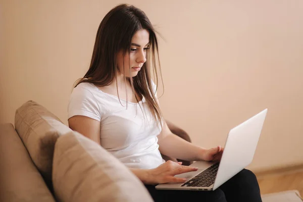 Молодая женщина работает дома в карантине. Женщина использует ноутбук на диване. Женское дистанционное обучение — стоковое фото
