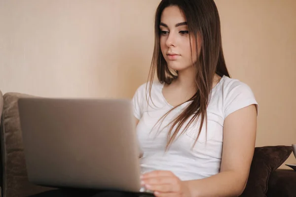 Jonge vrouw werkt thuis in quarantaine. Een vrouw gebruikt een laptop op de bank. Vrouwen studeren afstandsonderwijs — Stockfoto