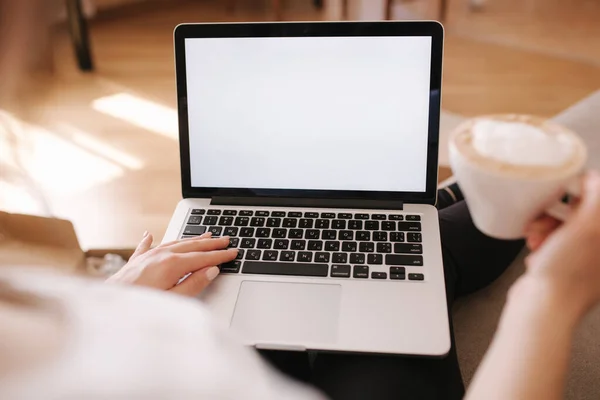 First person view of female working at home. Woman work on laptop and drink cappuccino. Mock up, white screen. Quarantine time