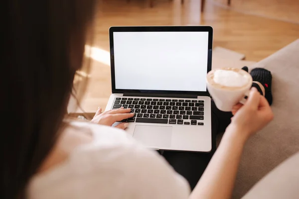 First person view of female working at home. Woman work on laptop and drink cappuccino. Mock up, white screen. Quarantine time