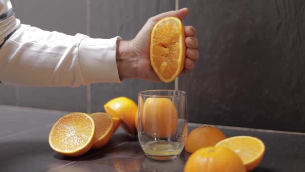 Ruka člověka vtlačuje šťávu z pomeranče do skla. Muž drží polovinu pomeranče po ruce — Stock video