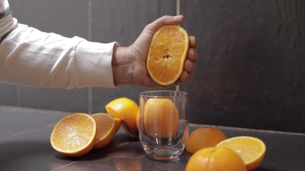 A mão do homem aperta o suco de uma laranja no vidro. Homem segurar metade de laranja na mão — Vídeo de Stock