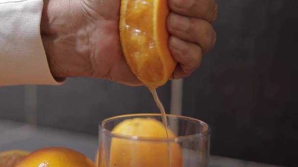 Ruka člověka vtlačuje šťávu z pomeranče do skla. Muž drží polovinu pomeranče po ruce — Stock video